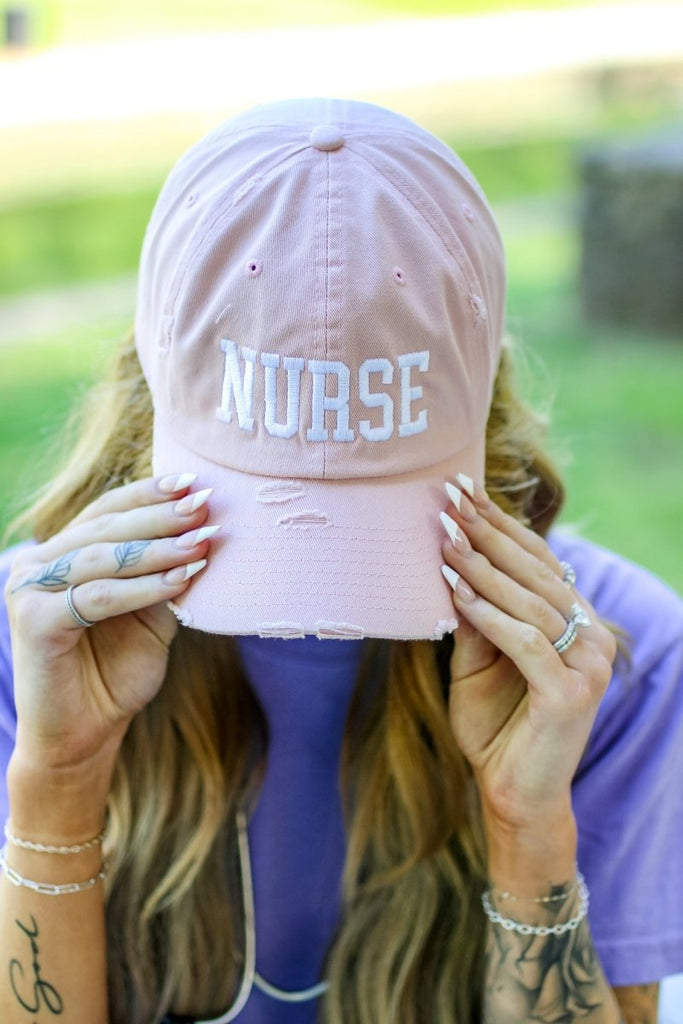 Rose colored distressed baseball cap with "NURSE" in white block letters