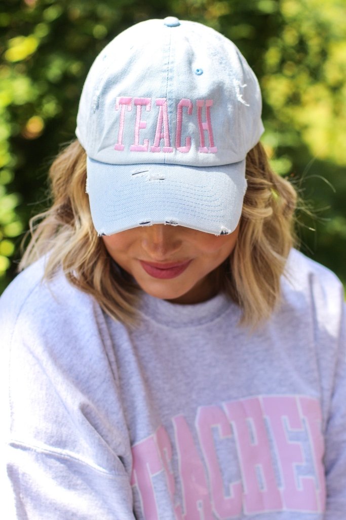 Light denim distressed adjustable baseball hat with light pink stitching with TEACH in block letters