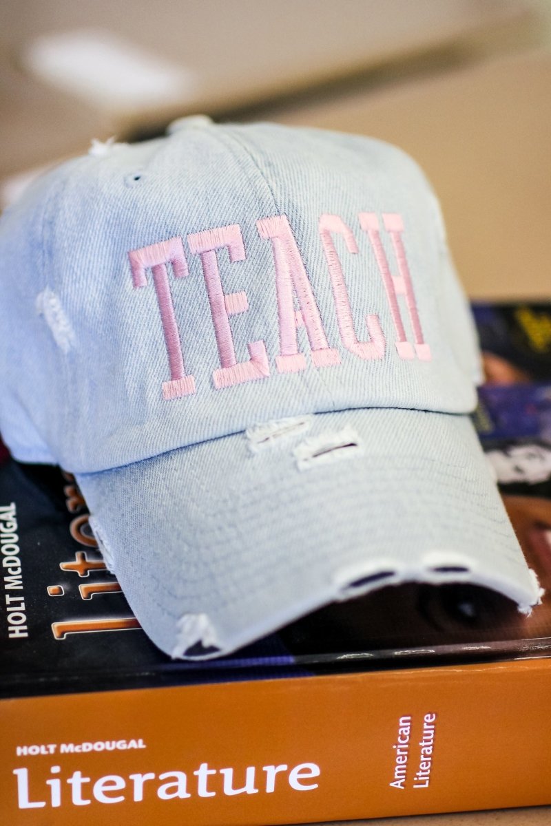 Light denim distressed adjustable baseball hat with light pink stitching with TEACH in block letters